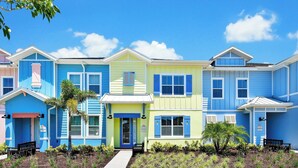 A row of colorful townhouses with a central entrance, small front yard, and benches.