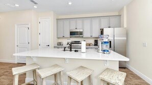 A kitchen with a large island, white cabinets, stainless steel appliances, and wooden stools.