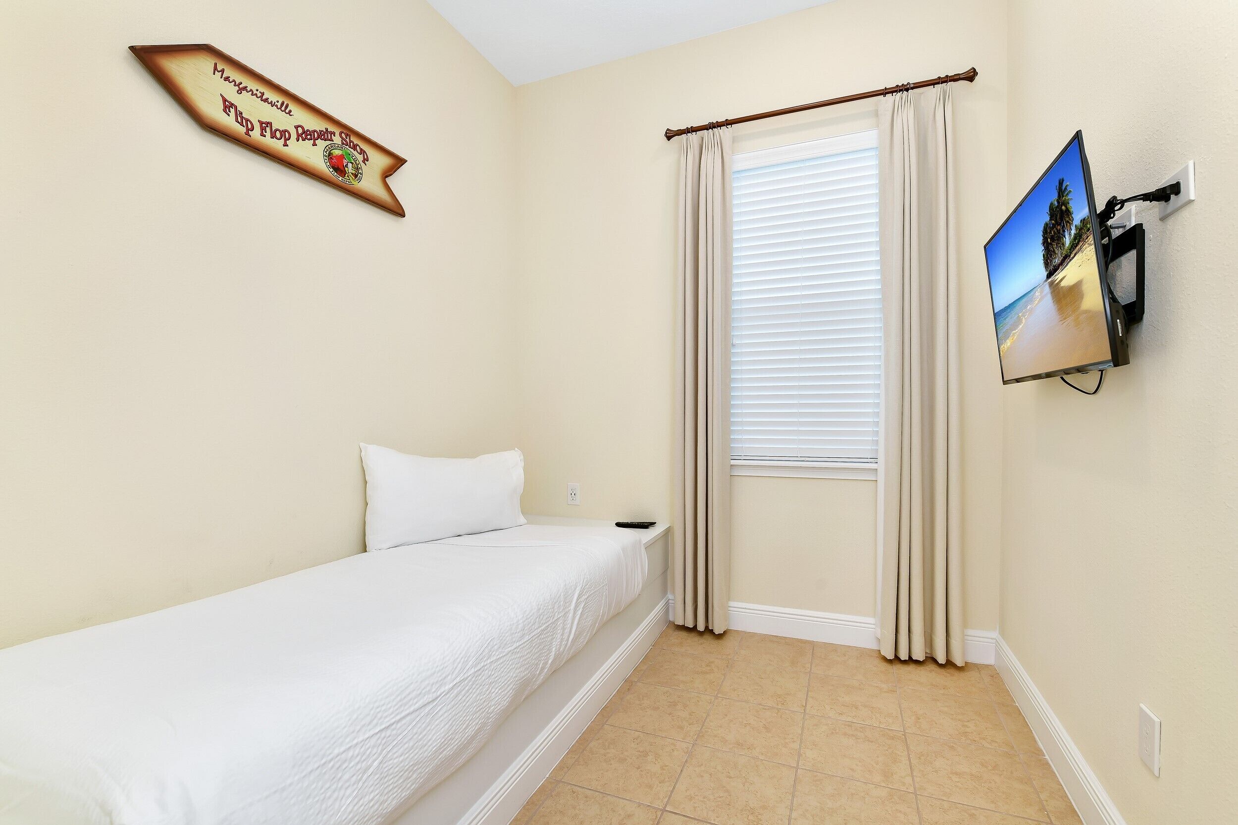 A hotel room with a bed, a TV mounted on the wall, a window with curtains, and a sign on the wall.