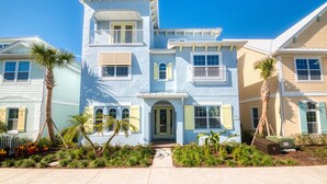 A two-story house with a balcony, a front door, and a small garden with palm trees.