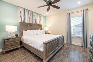 A bedroom with a wooden bed, two bedside tables with lamps, a ceiling fan, and a large window with curtains. - Vibrant Cottage near Disney | Private Pool + Resort & Waterpark Access - 8031KD (Kissimmee)