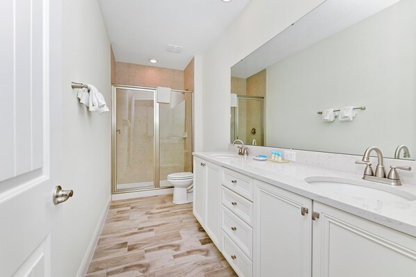 A modern bathroom with a glass shower enclosure, a white sink with a large mirror, and a beige tiled floor.