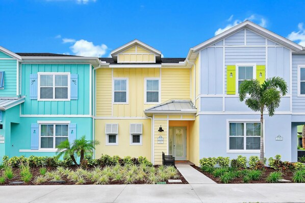 Una hilera de casas urbanas coloridas con un pequeño jardín delantero y un cielo azul despejado.