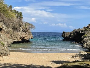 A coastal beach with rocky cliffs and clear blue water.