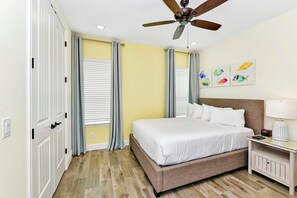 Un dormitorio con una cama, una mesita de noche, un ventilador de techo y una pared decorada con obras de arte.
