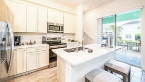 Una cocina moderna con gabinetes blancos, electrodomésticos de acero inoxidable y una isla grande con taburetes.