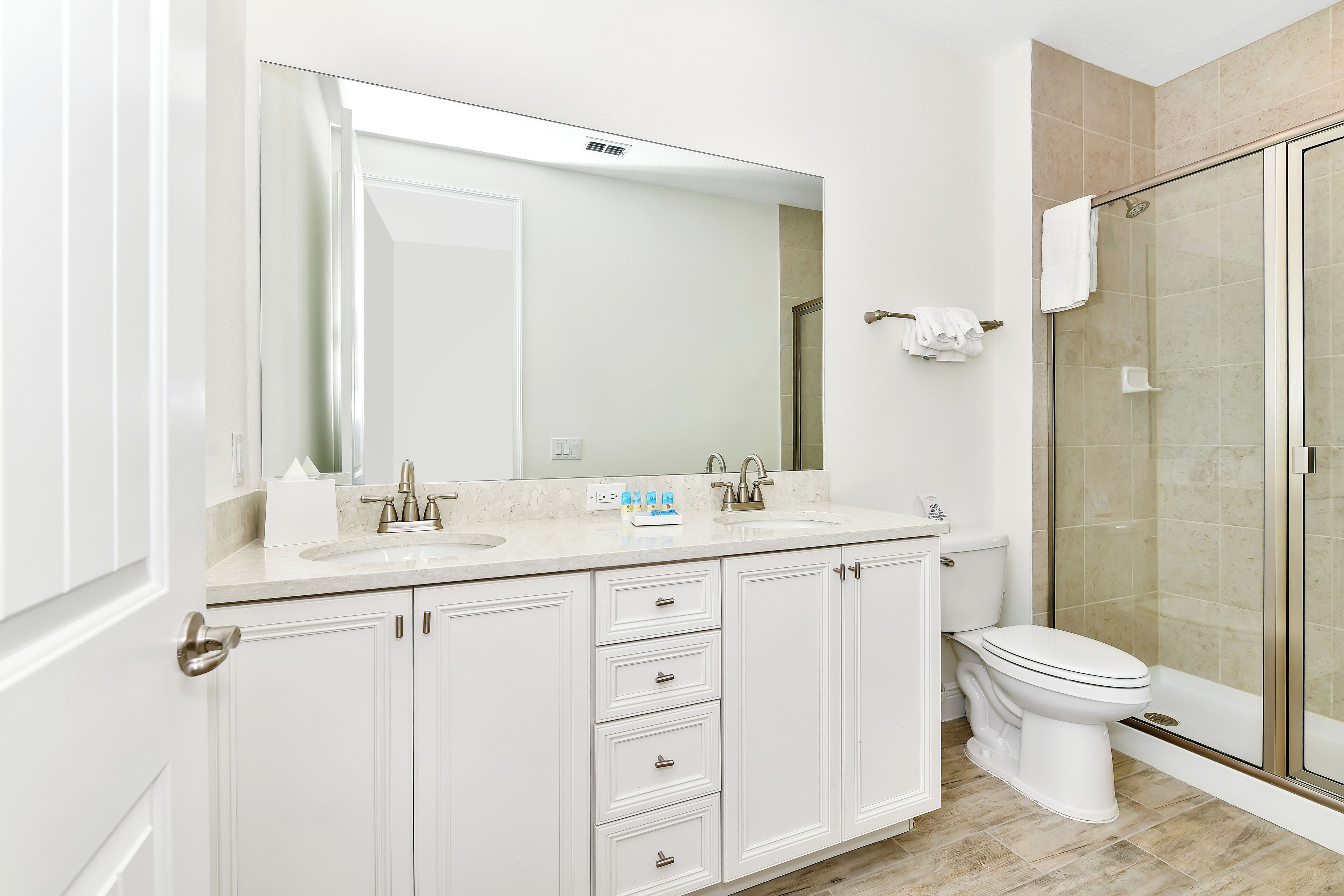 Un baño moderno con lavamanos doble, un espejo grande, inodoro y ducha con mampara de vidrio.