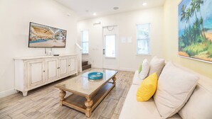 A spacious living room with a wooden coffee table, a white sofa with yellow pillows, a white cabinet, and a large painting on the wall. - Inviting Cottage with Private Hot Tub near Disney with Margaritaville Resort &. (Kissimmee)