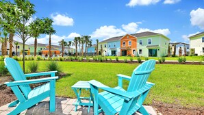 A row of colorful houses with a lawn and two turquoise Adirondack chairs. - Colorful Villa near Disney | Margaritaville & Waterpark Access - 3140CS (Kissimmee)
