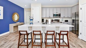 Una cocina moderna con armarios blancos, un refrigerador de acero inoxidable y una isla central con taburetes de bar.