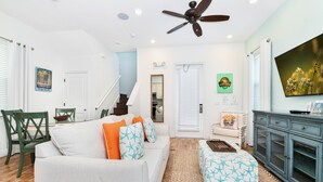A living room with a sofa, ottoman, and a television. There is a staircase leading to another level. - Crystal Cottage near Disney with Margaritaville Resort & Island H2O Access -. (Kissimmee)