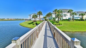 A wooden boardwalk leading to a row of beachfront condos with palm trees and a clear blue sky. - Beautiful Waterfront Cottage with Private Pool near Disney with Margaritaville. (Kissimmee)