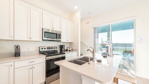 Cocina moderna con armarios blancos, electrodomésticos de acero inoxidable y un amplio ventanal con vista a una piscina.