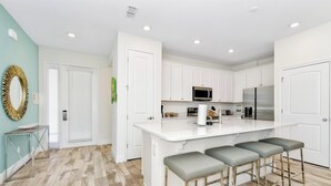 Una cocina moderna con armarios blancos, una isla central con taburetes de bar, un microondas y un refrigerador.