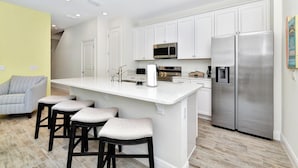 Una cocina moderna con armarios blancos, electrodomésticos de acero inoxidable y una isla central con taburetes.