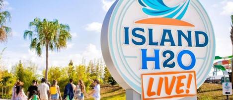Une enseigne avec l’inscription « ISLAND H2O LIVE ! », entourée de palmiers et de personnes.