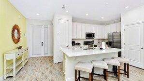 A modern kitchen with white cabinetry, a central island with bar stools, and a herringbone-patterned floor.