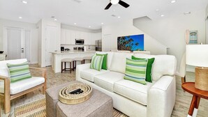 A modern living room with a white sofa, green and white striped pillows, a coffee table with a remote control, and a ceiling fan.