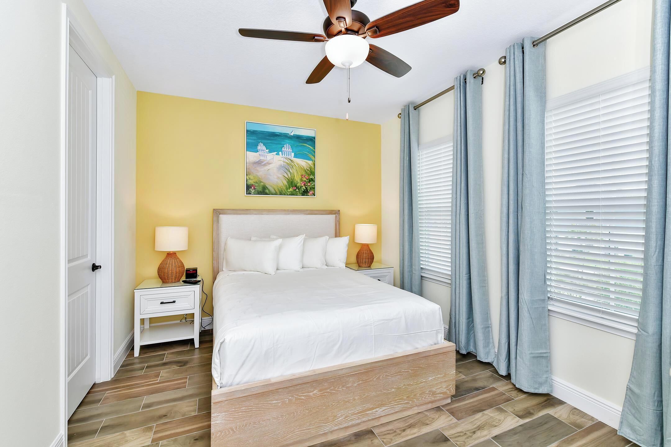 Une chambre à coucher avec un lit, des tables de chevet, un ventilateur de plafond et un tableau accroché au mur.
