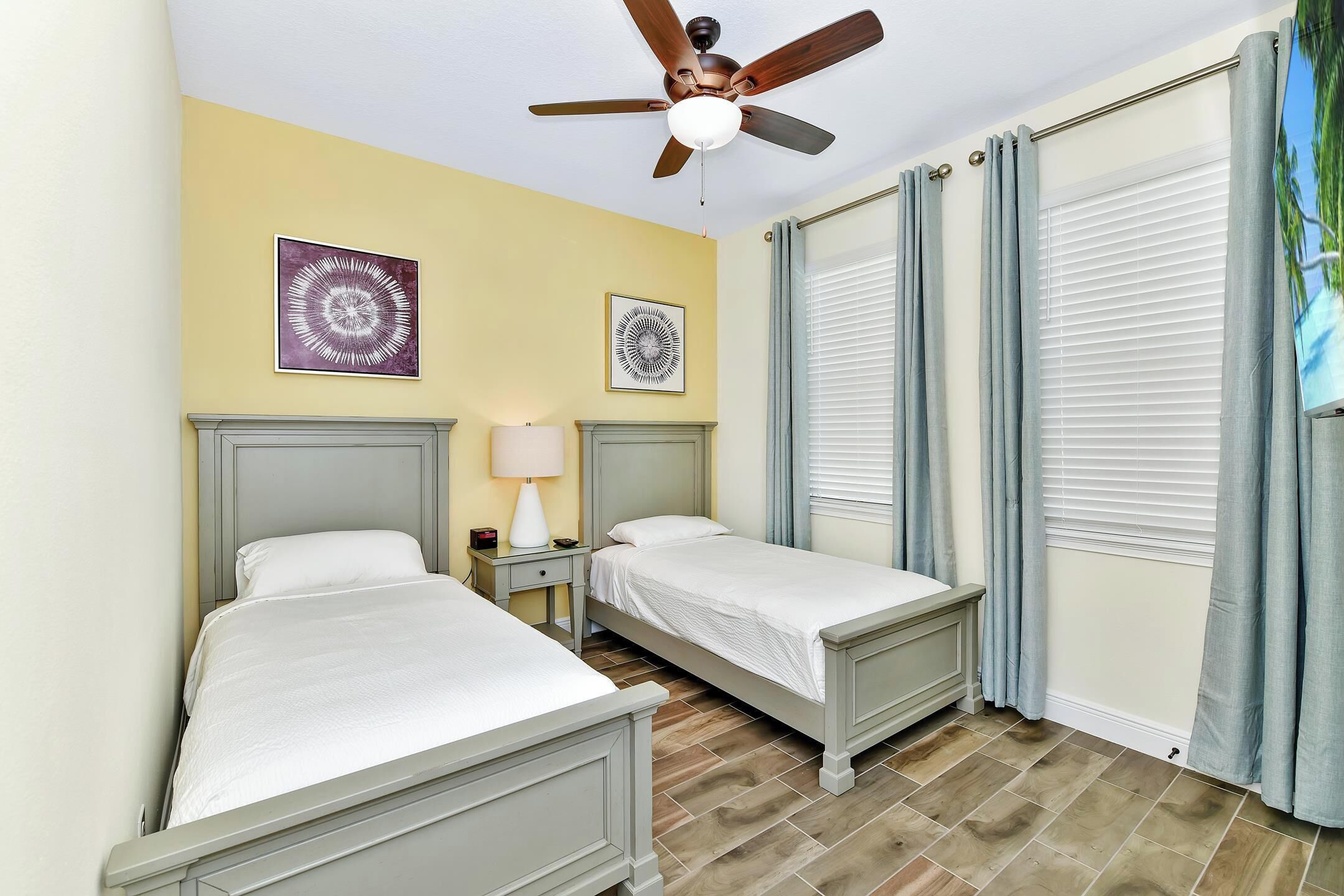 A bedroom with two beds, a ceiling fan, and a window with curtains.