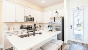 Una cocina moderna con muebles blancos, electrodomésticos de acero inoxidable y una isla grande con asientos.