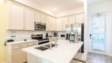 A modern kitchen with white cabinetry, stainless steel appliances, and a large island with a sink.
