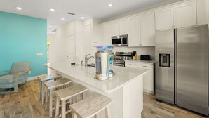 Una cocina moderna con armarios blancos, electrodomésticos de acero inoxidable y una isla central con taburetes.