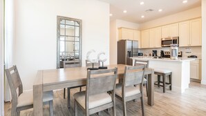 A modern kitchen with light-colored cabinets, a central island, and a dining area with wooden chairs and a table.