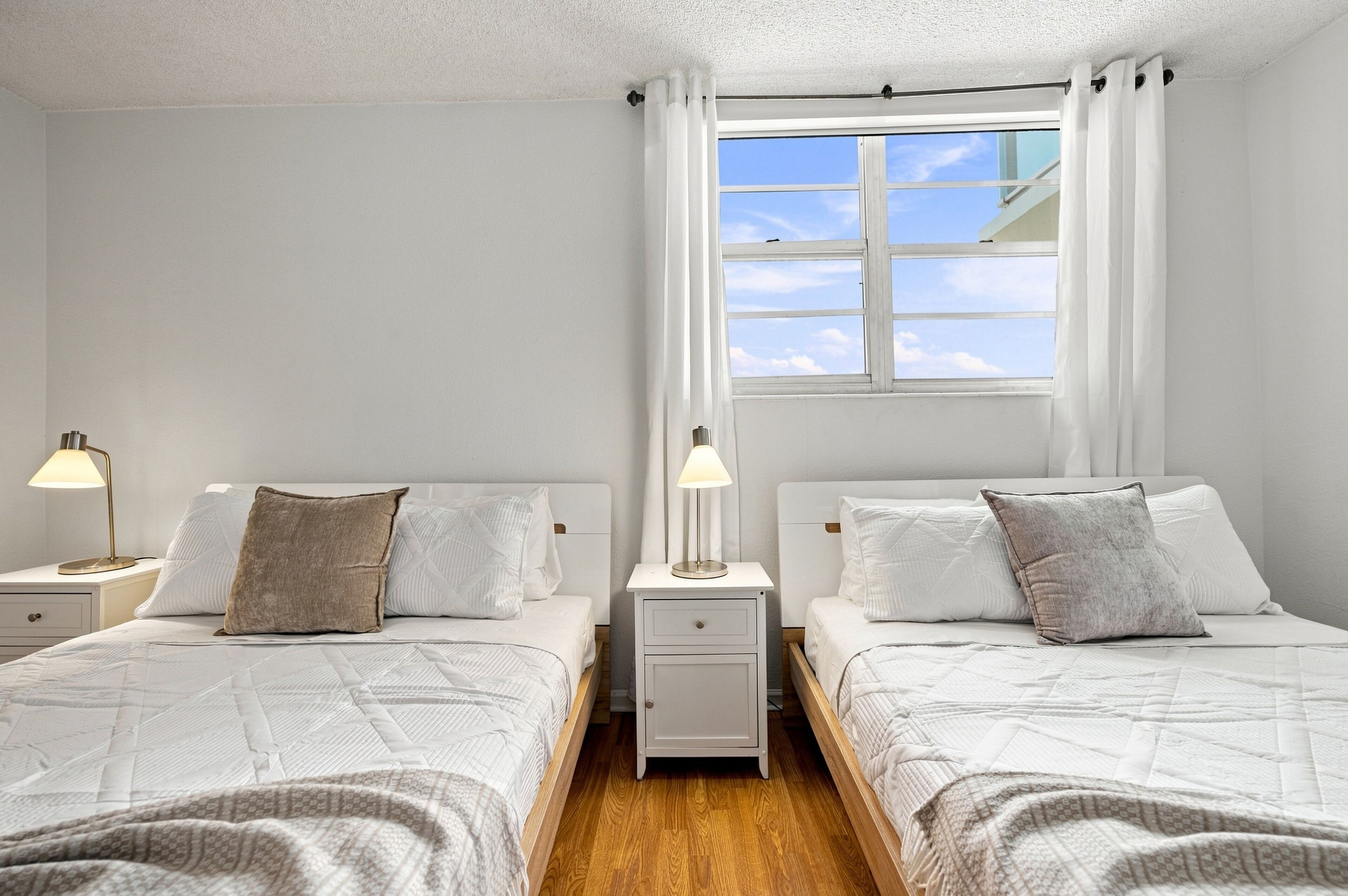 A double room with two beds, a window with curtains, bedside lamps, and a wooden floor.