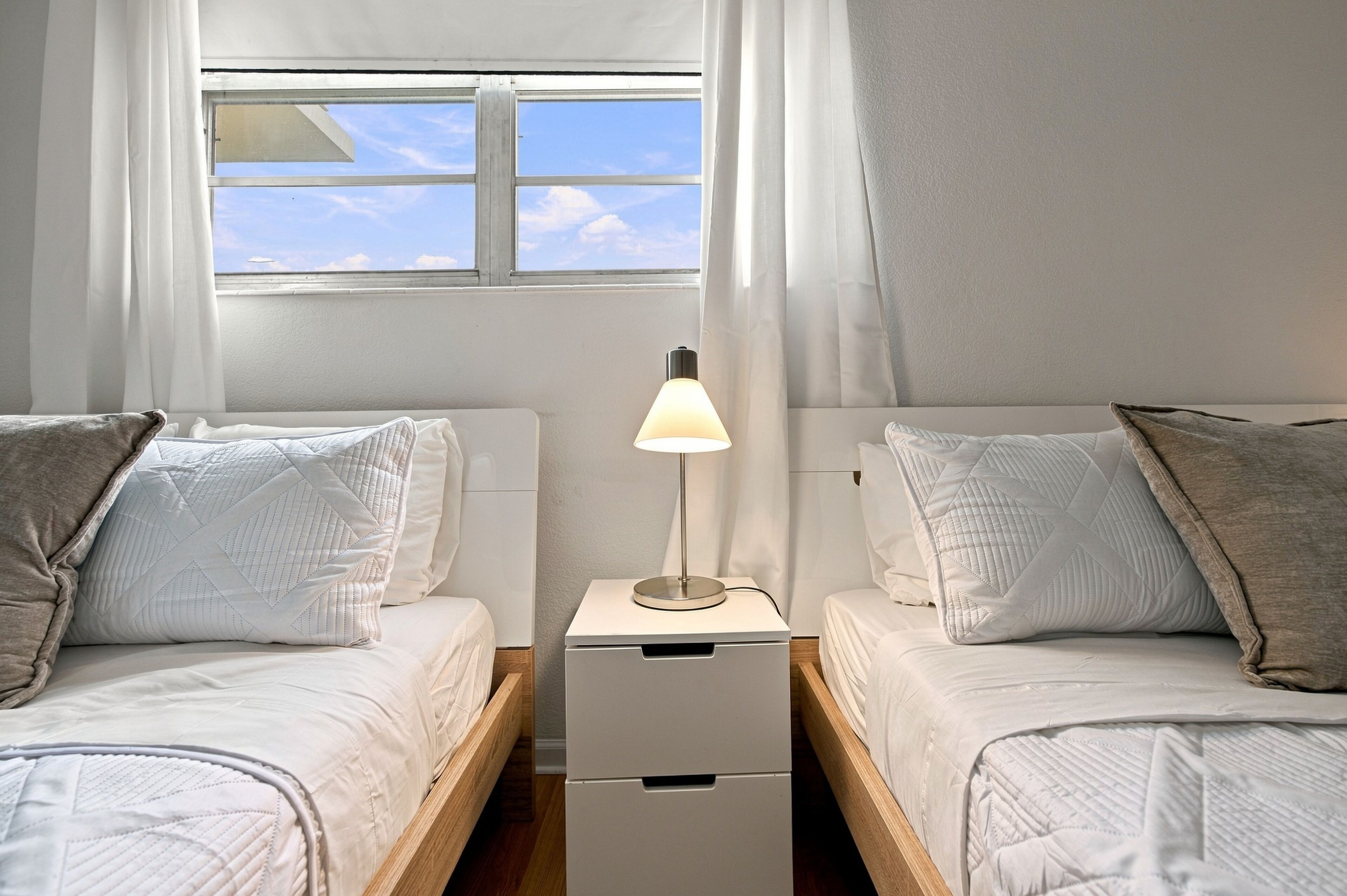 A bedroom with two beds, a nightstand with a lamp, and a window with curtains.