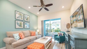 A living room with a beige sofa, orange ottoman, teal armchair, and a ceiling fan. - Blue Sky Cottage near Disney with Private Pool & Margaritaville Resort and. (Kissimmee)