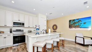 A modern kitchen with white cabinets, a large island with stools, a microwave, and a water dispenser. - Perfect Family Villa near Disney | Margaritaville & Waterpark Access - 3168CS (Kissimmee)