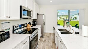 A modern kitchen with white cabinets, stainless steel appliances, a large window with a view of houses, and a countertop with a coffee maker.