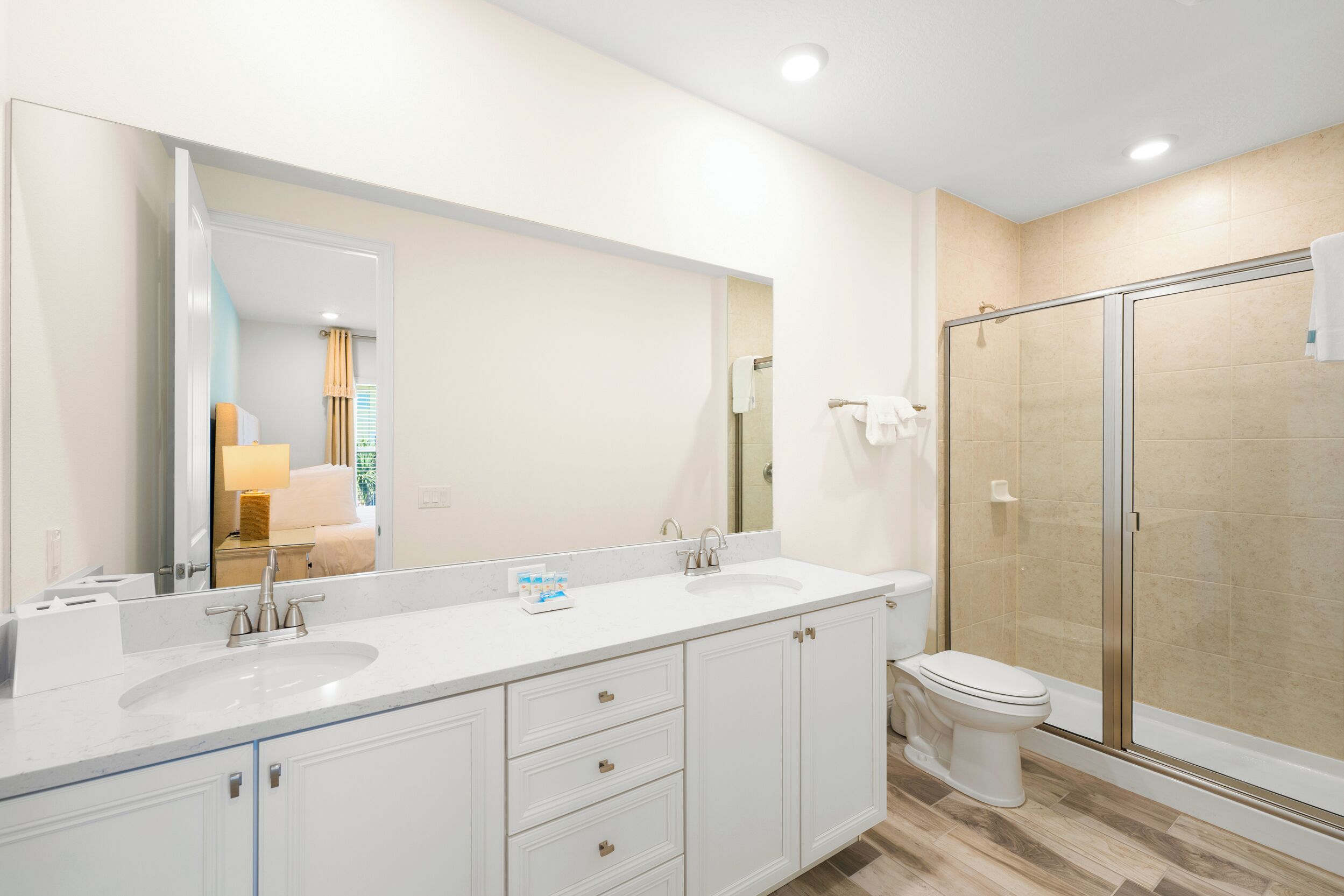 A modern bathroom with a large mirror, two sinks, a toilet, and a glass-enclosed shower.