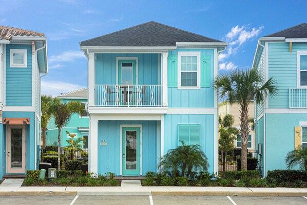 A two-story residential building with a balcony, a front door, and a small porch area. - Sea Shell Blue Cottage near Disney | Pool + Resort & Waterpark - 8039KD (Kissimmee)