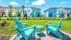 Una hilera de casas coloridas con césped y dos sillas Adirondack turquesas al frente.