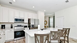 A modern kitchen with white cabinetry, a central island with bar stools, a built-in oven, and a refrigerator. - Sunny Villa near Disney | Resort & H2O Waterpark Access - 8170CP (Kissimmee)
