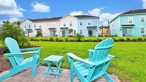 Una hilera de casas coloridas con césped y dos sillas Adirondack turquesas.