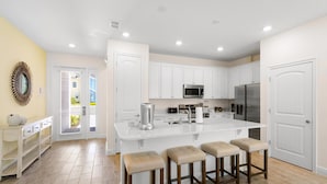 A modern kitchen with white cabinetry, a large island with stools, and stainless steel appliances. - Beach Blessing Villa near Disney | Margaritaville & Waterpark Access - 3204CS (Kissimmee)