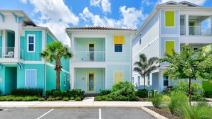 A row of colorful, two-story townhouses with balconies, a clear sky, and a well-maintained front yard. - Sandy Toes Cottage with Private Pool near Disney and Margaritaville Resort &. (Kissimmee)