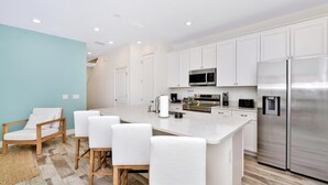 Une cuisine moderne avec des meubles blancs, un réfrigérateur en acier inoxydable, un four à micro-ondes et un grand îlot central doté de tabourets de bar.