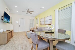 A modern dining area with a glass table, grey upholstered chairs, and a ceiling fan.