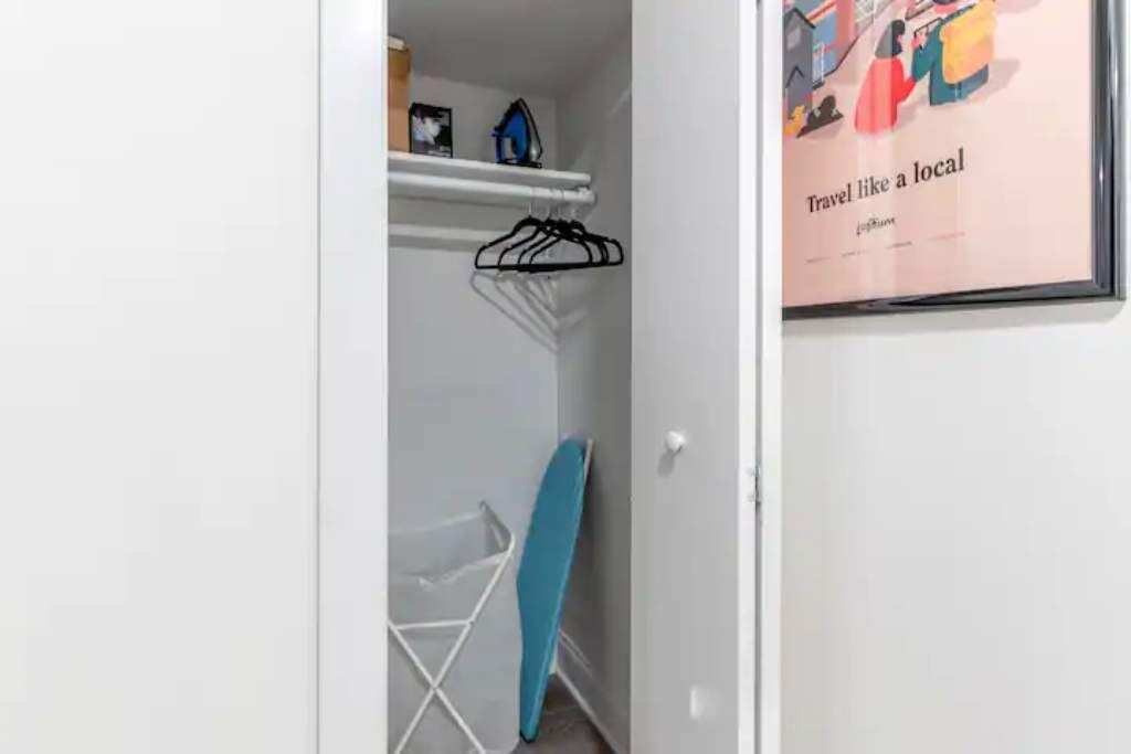 Une pièce avec une porte blanche, un tableau encadré accroché au mur et une planche à repasser bleue appuyée contre le mur.