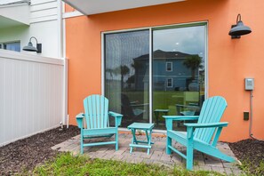 Un espace patio avec deux fauteuils Adirondack turquoise et une petite table, une porte-fenêtre coulissante et une clôture blanche.