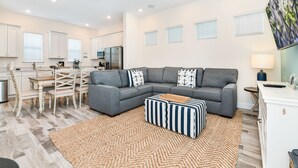 Ein modernes Wohnzimmer mit einem grauen Ecksofa, einem Holzesstisch und einer Küche im Hintergrund.