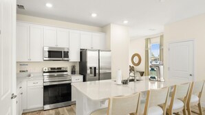 Een moderne keuken met witte kasten, roestvrijstalen apparatuur en een centraal eiland met stoelen.