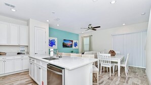 A modern kitchen with white cabinetry, a central island, and a dining area with white chairs and a table.