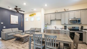 Cocina moderna con armarios grises, microondas y estufa. Cuenta con un comedor con mesa y sillas de madera.