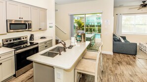 A modern kitchen with a central island, stainless steel appliances, and a view to a backyard with a pool and outdoor seating.