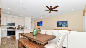 Une cuisine moderne avec des meubles blancs, une table à manger en bois et un ventilateur de plafond.